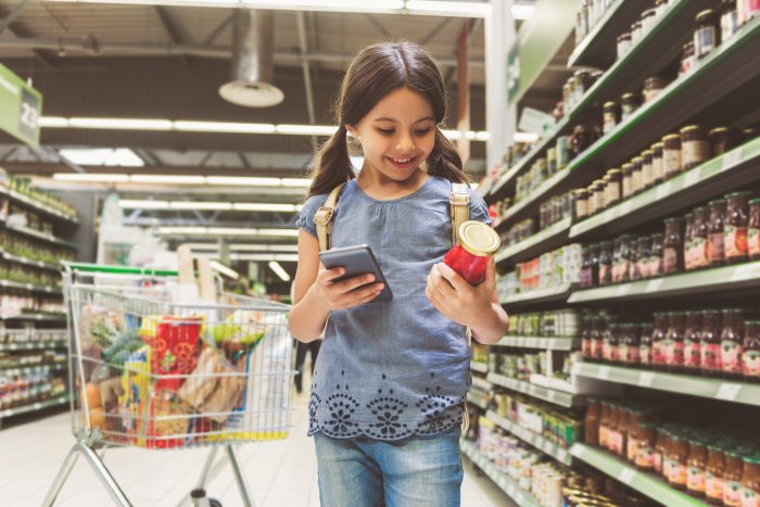 kind in de supermarkt met in de ene hand etenswaren en in de andere hand een smartphone